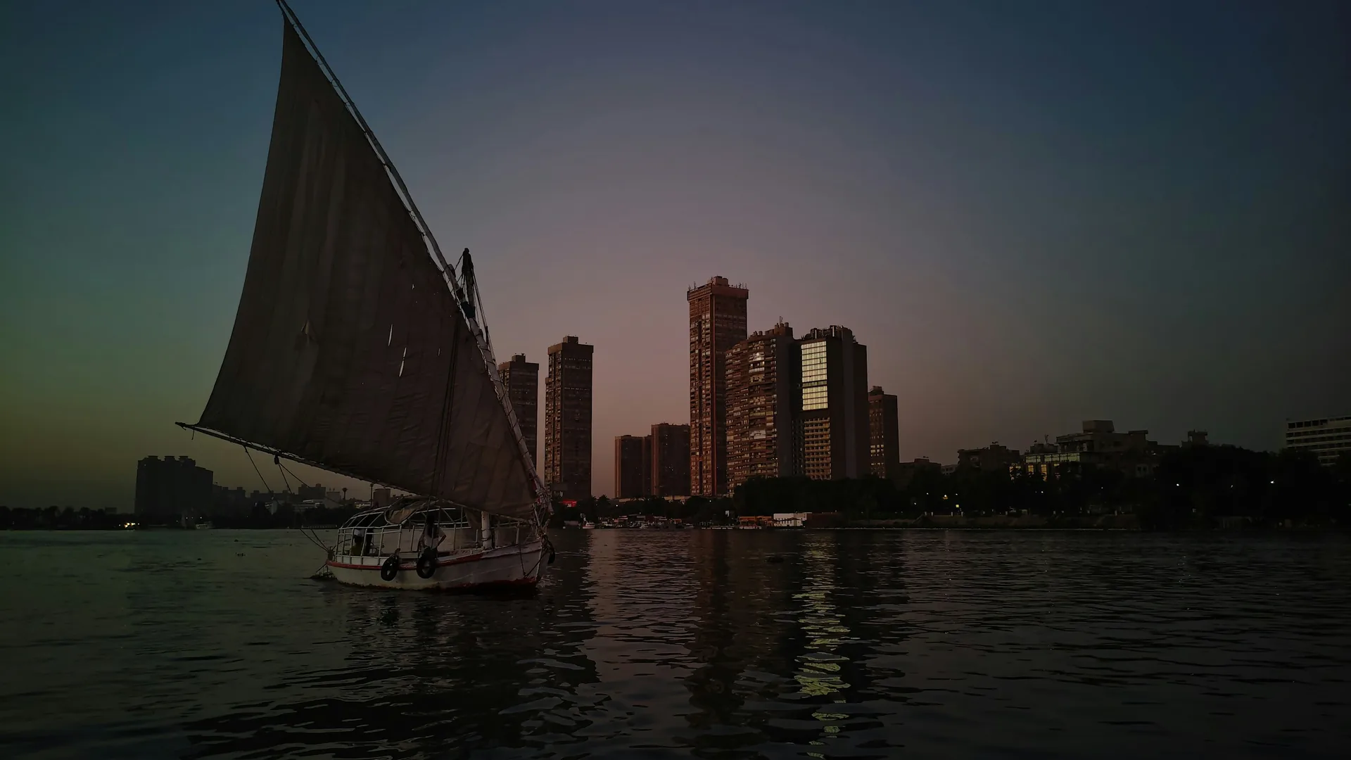 A traditional felucca sailing the Nile at dusk with Cairo's high-rise skyline behind it